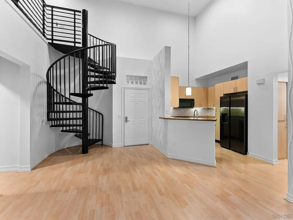 Modern California interior with black spiral staircase, light wood floors, and kitchen with light cabinets and black appliances.