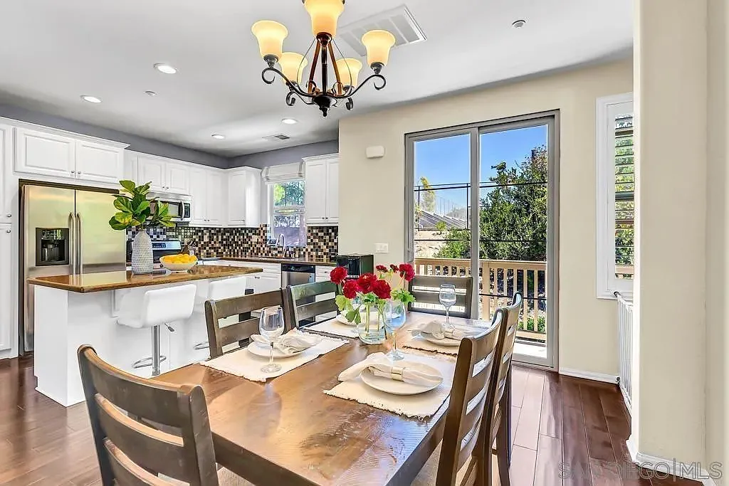 California kitchen and dining area with wooden table, white cabinets, island with stools, and window view.